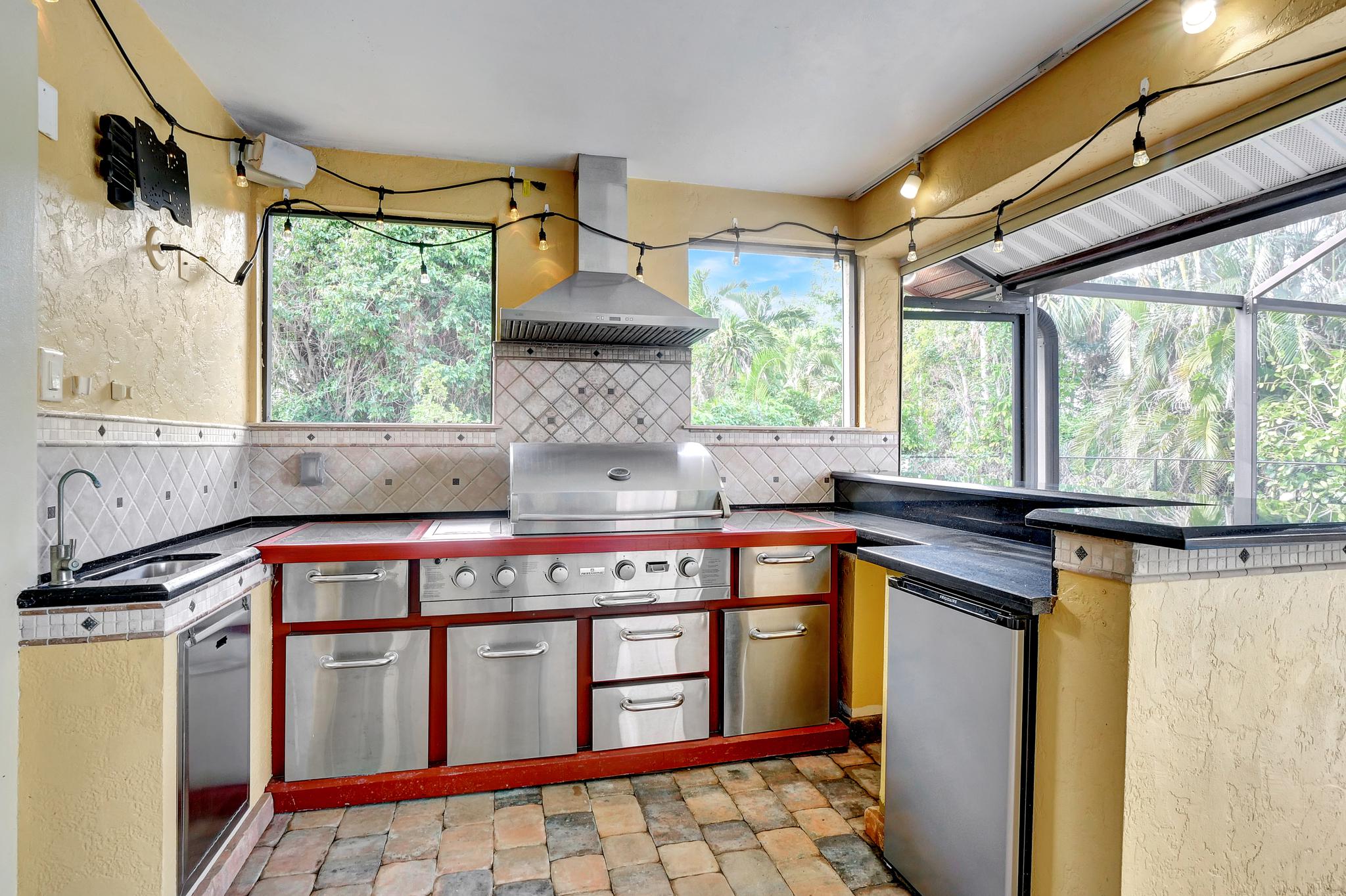 There is a High End Outdoor Kitchen With a Propane Gas Grill, Sink, Hood, Mini Fridge and Prep Space